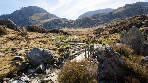 View of Snowdonia with mountains in the background and a rocky landscape and wooden bridge in the mid ground